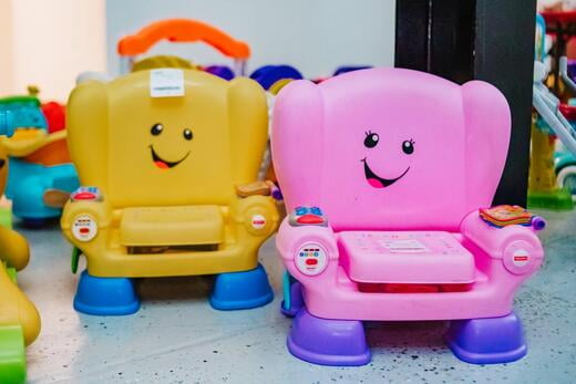 A yellow potty seat next to a pink potty seat. Both potty seats have smiley faces on the back-rest.